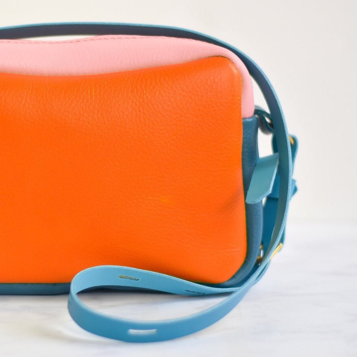 Orange and pink handbag with a blue strap on a white background