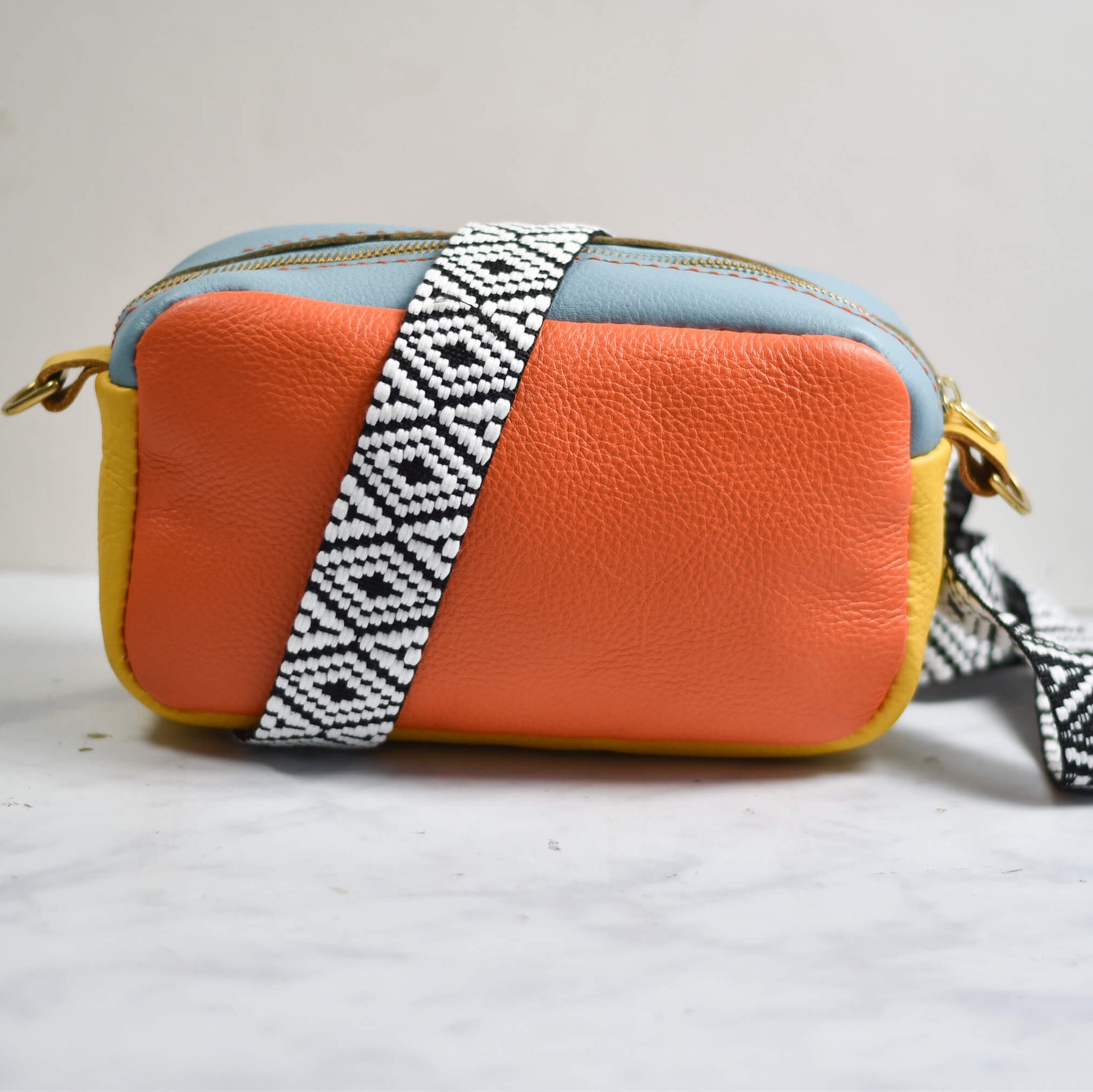Orange crossbody bag with a patterned strap on a light gray background