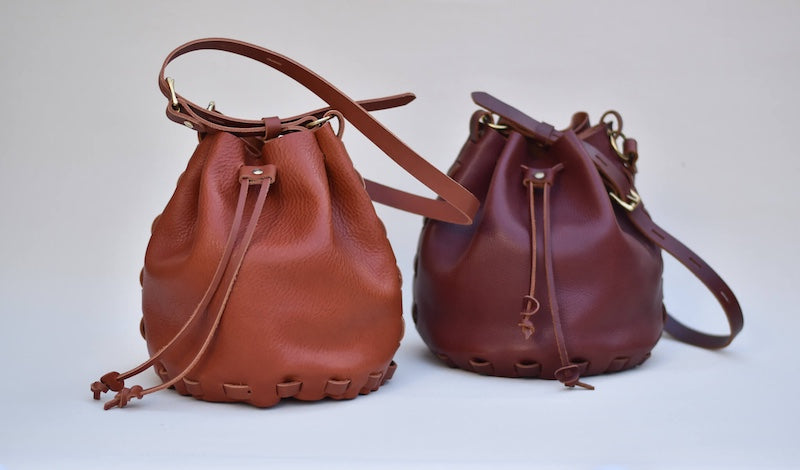 two leather bucket bags side by side one is tan leather the other is burgandy leather both made from a no sew bag making kit