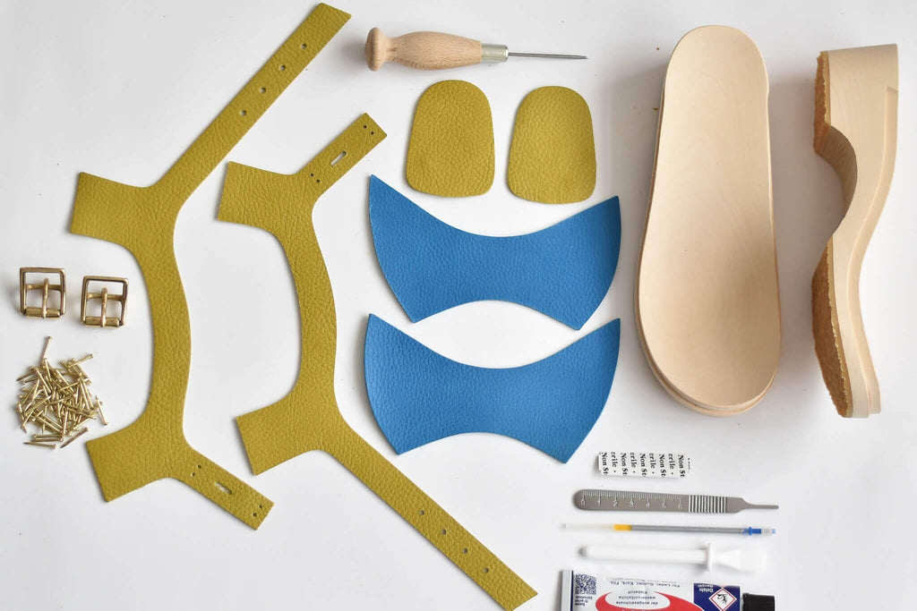 Contents of DIY leather shoe making kit — leather pieces, buckles, tacks, awl, glue, craft knife and wooden soles