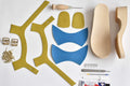 Contents of DIY leather shoe making kit — leather pieces, buckles, tacks, awl, glue, craft knife and wooden soles