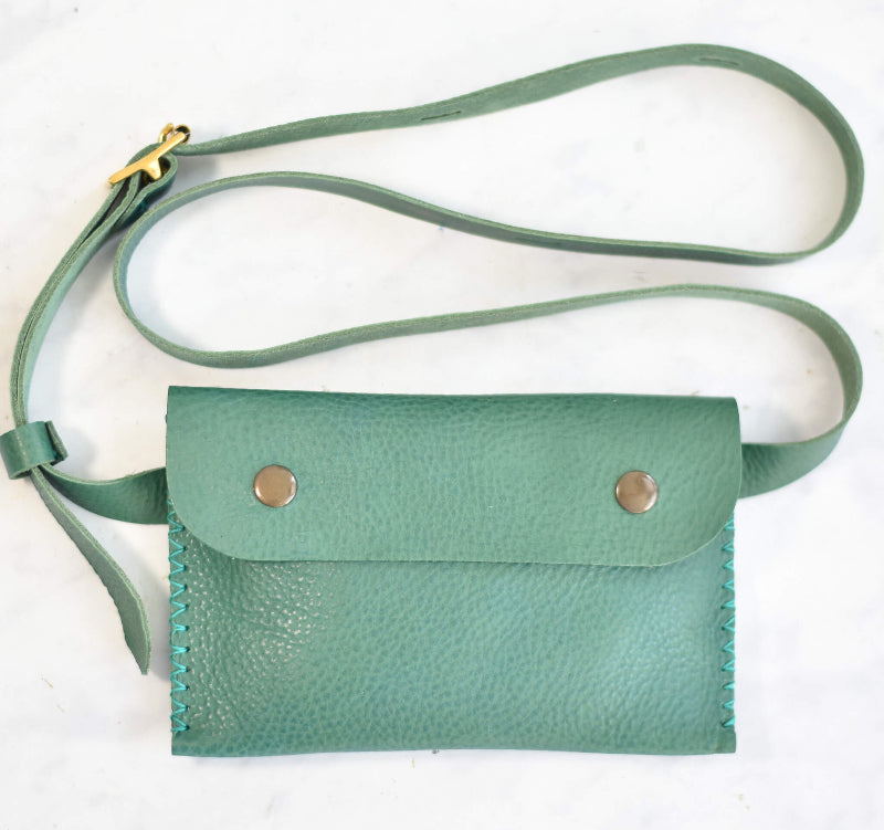 Green leather crossbody bag with strap on a white background