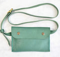 Green leather crossbody bag with strap on a white background