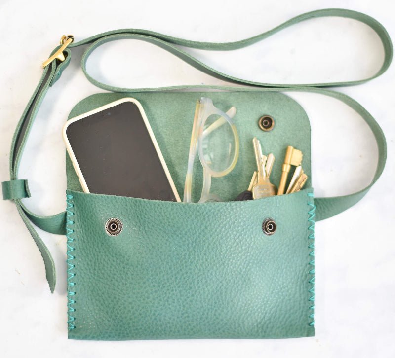 Green crossbody bag with phone, glasses, and clips on a white background