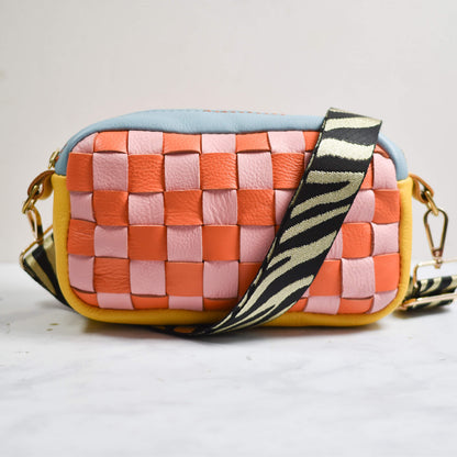 Colorful woven handbag with a zebra-striped strap on a light background