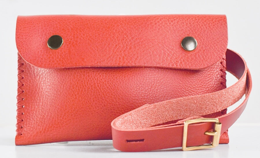 A coral belt bag with a shoulder strap and buckle closure, displayed on a white background.