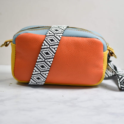 Orange crossbody bag with a patterned strap on a light gray background