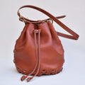 A tan leather bucket bag with a drawstring top and a shoulder strap made from a make at home kit.
