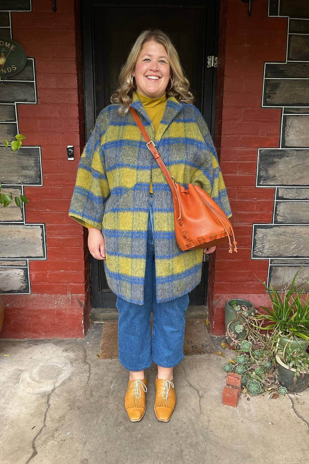 woman wearing tan leather bag she made smiling in front of front door
