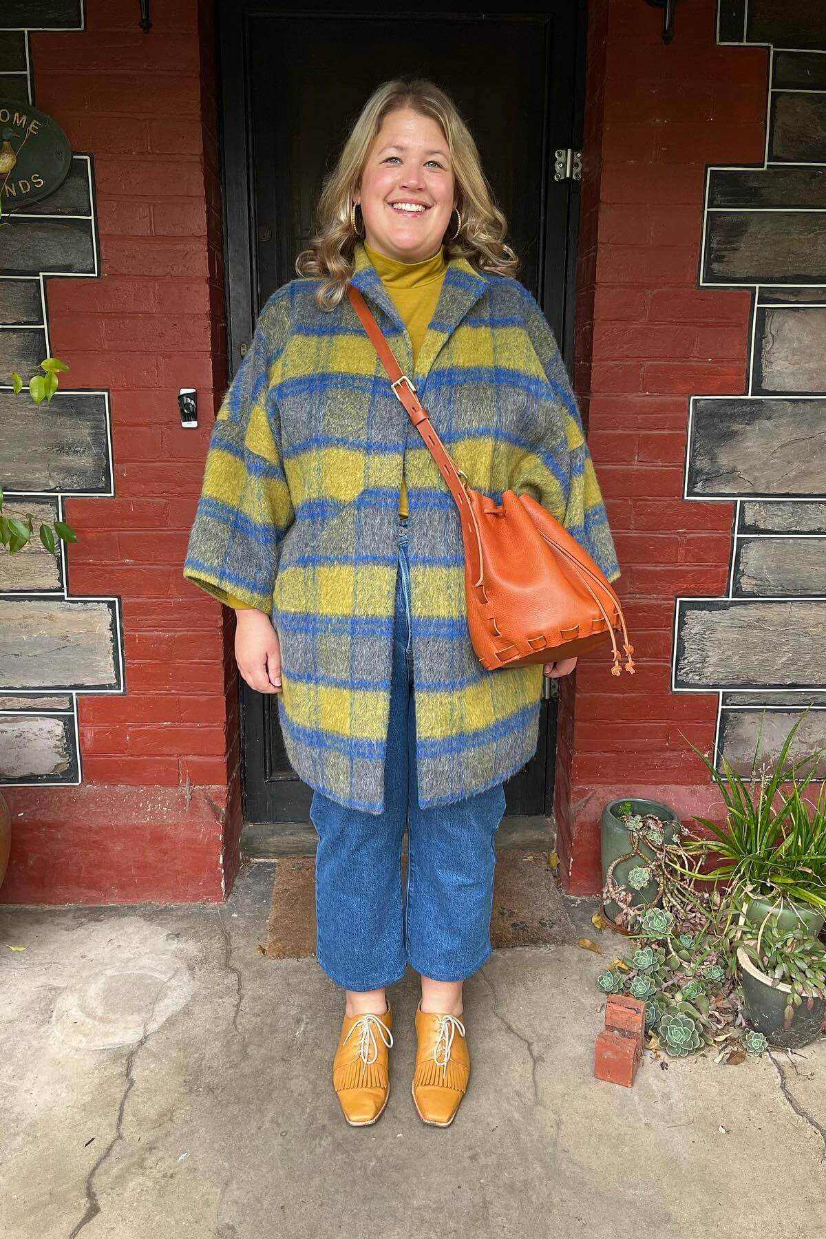 woman wearing tan leather bag she made smiling in front of front door