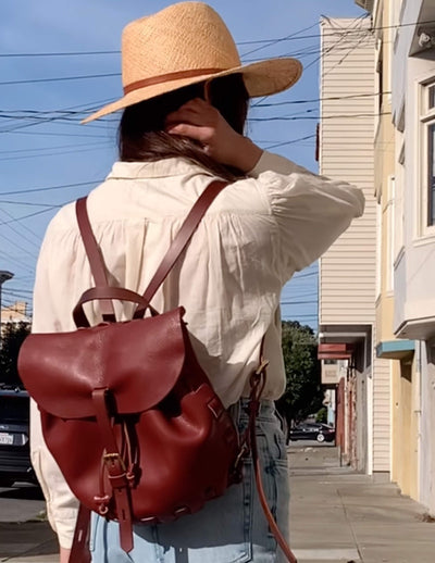 Person wearing a straw hat and red backpack on a city street